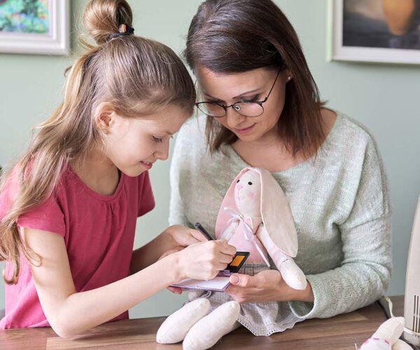 Mother and daughter child play together at home Mother and daughter child play together at home, girl and mom make make-up paints cheeks to toy handmade doll bunny sewn on sewing machine